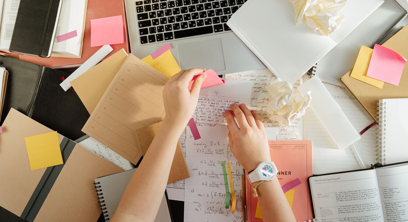 Vue de dessus d'un espace de travail avec des livres, un ordinateur portable et des mains organisant des notes à l'aide de post-it