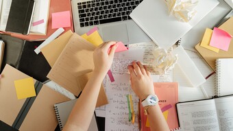 Vue de dessus d'un espace de travail avec des livres, un ordinateur portable et des mains organisant des notes à l'aide de post-it